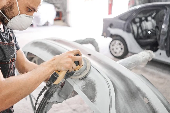Person schleift Autoteil mit Schleifmaschine